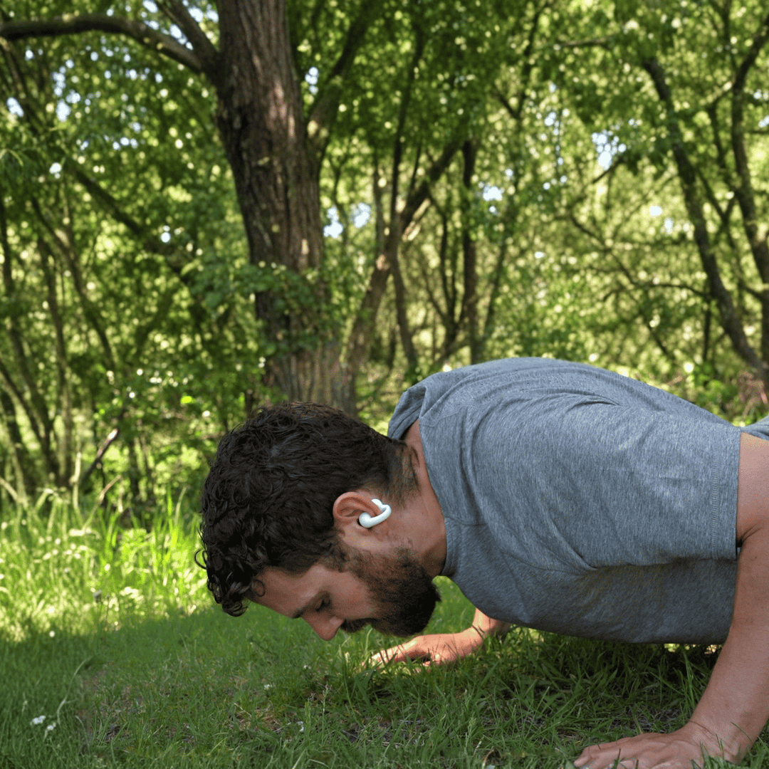 Man doing push-ups on grass wearing a white Gibutech Ultra Open earbud