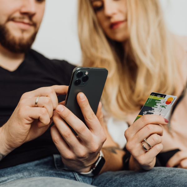 Couple on a sofa paying for an online order on a smartphone with a bank card