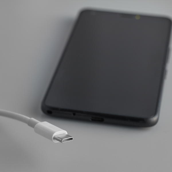 Smartphone lying on a grey surface with a white USB-C cable beside its charging port