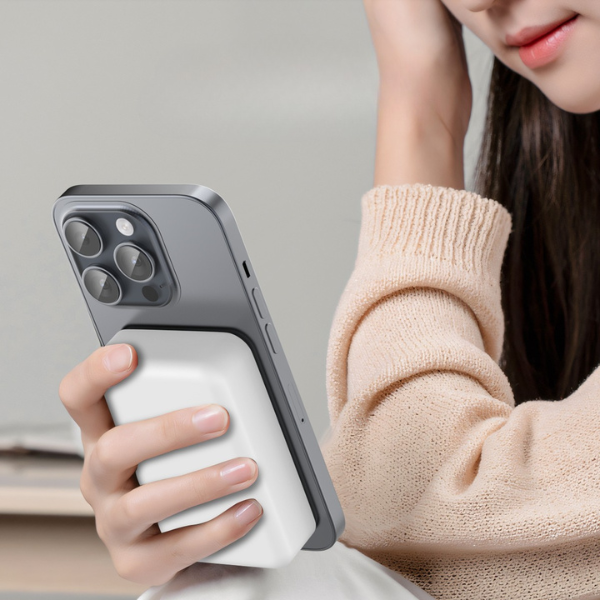 Woman holding an iPhone with a white magnetic power bank attached to the back