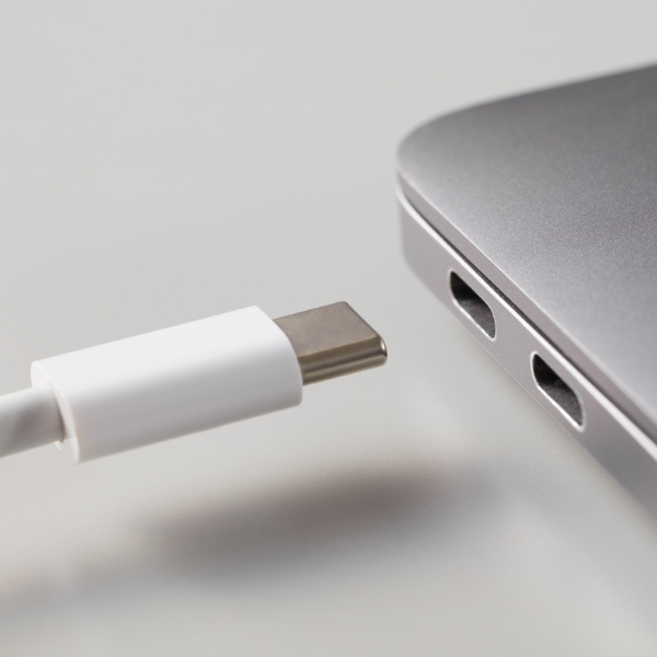 White USB-C cable about to plug into the side of a laptop
